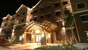 Un hotel Staybridge Suites con fachada de piedra, varios balcones y una entrada bien iluminada.