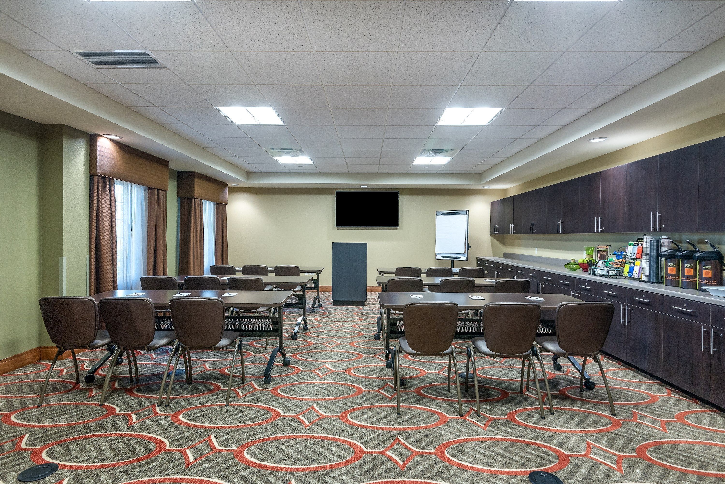 A conference room with a large table, chairs, a projector screen, and a kitchenette area.