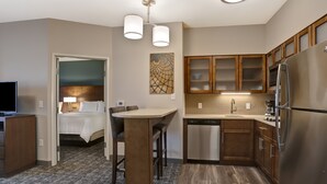A modern kitchen with wooden cabinets, a stainless steel refrigerator, and a dining area with a table and chairs. - Flexible 1-Bedroom Suite w/ Full Kitchen, KS (Overland Park)