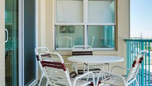 Un balcon avec une table et des chaises, une porte-fenêtre coulissante et une vue sur la rue.
