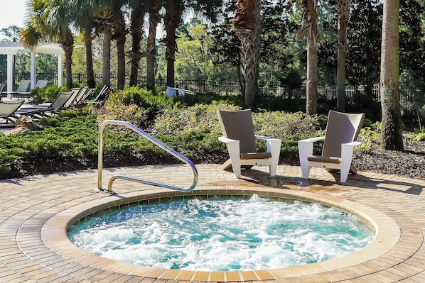 A hot tub surrounded by lounge chairs and a poolside area with a brick walkway.