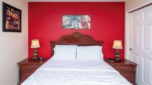 A hotel room with a red accent wall, a classic wooden bed, two bedside tables with lamps, and a framed picture above the bed.