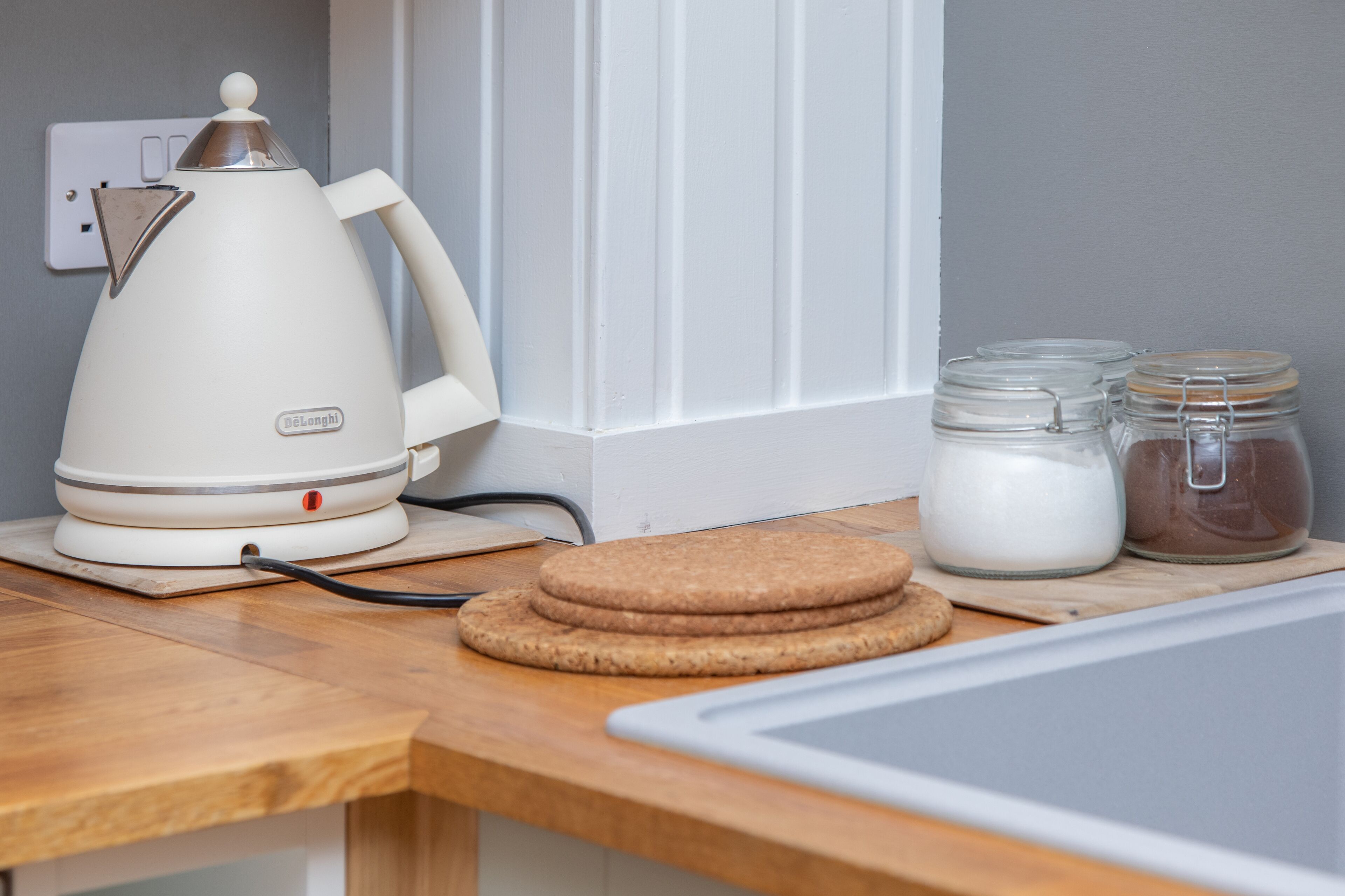 Un plan de travail de cuisine avec une bouilloire électrique blanche, une pile de biscuits bruns et deux bocaux en verre avec des couvercles.