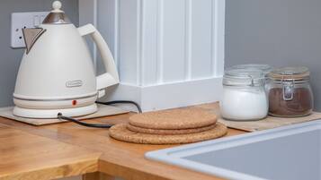 Un plan de travail de cuisine avec une bouilloire électrique blanche, une pile de biscuits bruns et deux bocaux en verre avec des couvercles.