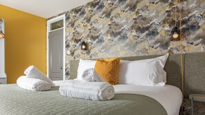 Una cama bien hecha con almohadas blancas y mostaza, un edredón verde y toallas blancas enrolladas.