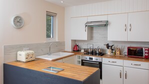Una cocina moderna con armarios blancos, encimera de madera, horno empotrado, microondas y un reloj en la pared.