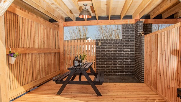 Una terraza de madera con una mesa de picnic, un muro de ladrillo y una valla de madera.
