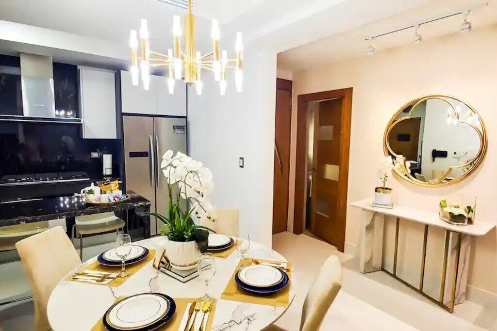 A modern kitchen with a dining area, featuring a chandelier, a round mirror, and a dining table set for four.