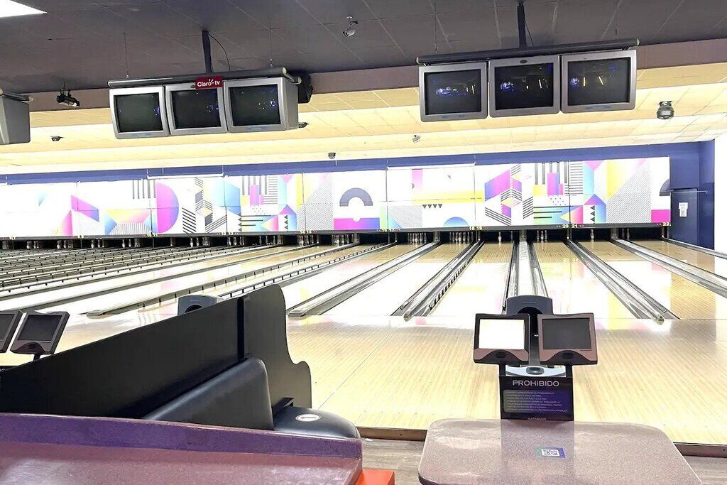 Un bowling avec plusieurs pistes, un panneau indiquant « DÉFENDU » et plusieurs téléviseurs fixés au plafond.