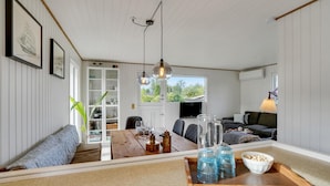A cozy living room with a sofa, a dining table with glassware, a TV, and a bookshelf. - Nice home in Kerteminde with WiFi (Kerteminde)