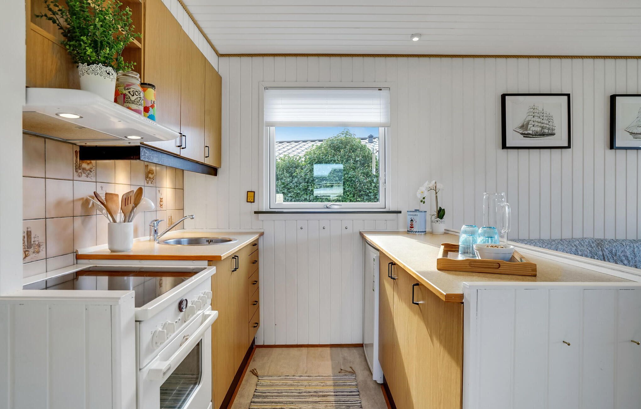 A compact kitchen with white cabinetry, a built-in oven, and a window with a view of greenery.