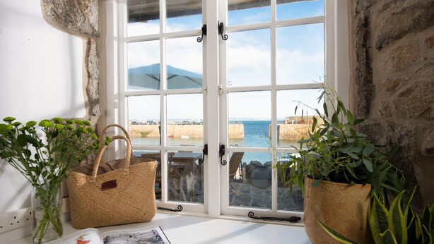 Een kamer aan de kust met een groot raam met uitzicht op de zee, stenen muren en twee rieten manden op de vensterbank.
