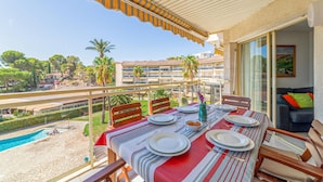 Ein Balkon mit Esstisch, mit Blick auf einen Pool und eine Wohngegend mit Palmen.