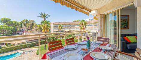 A balcony with a table set for dining, overlooking a pool and a residential area with palm trees.