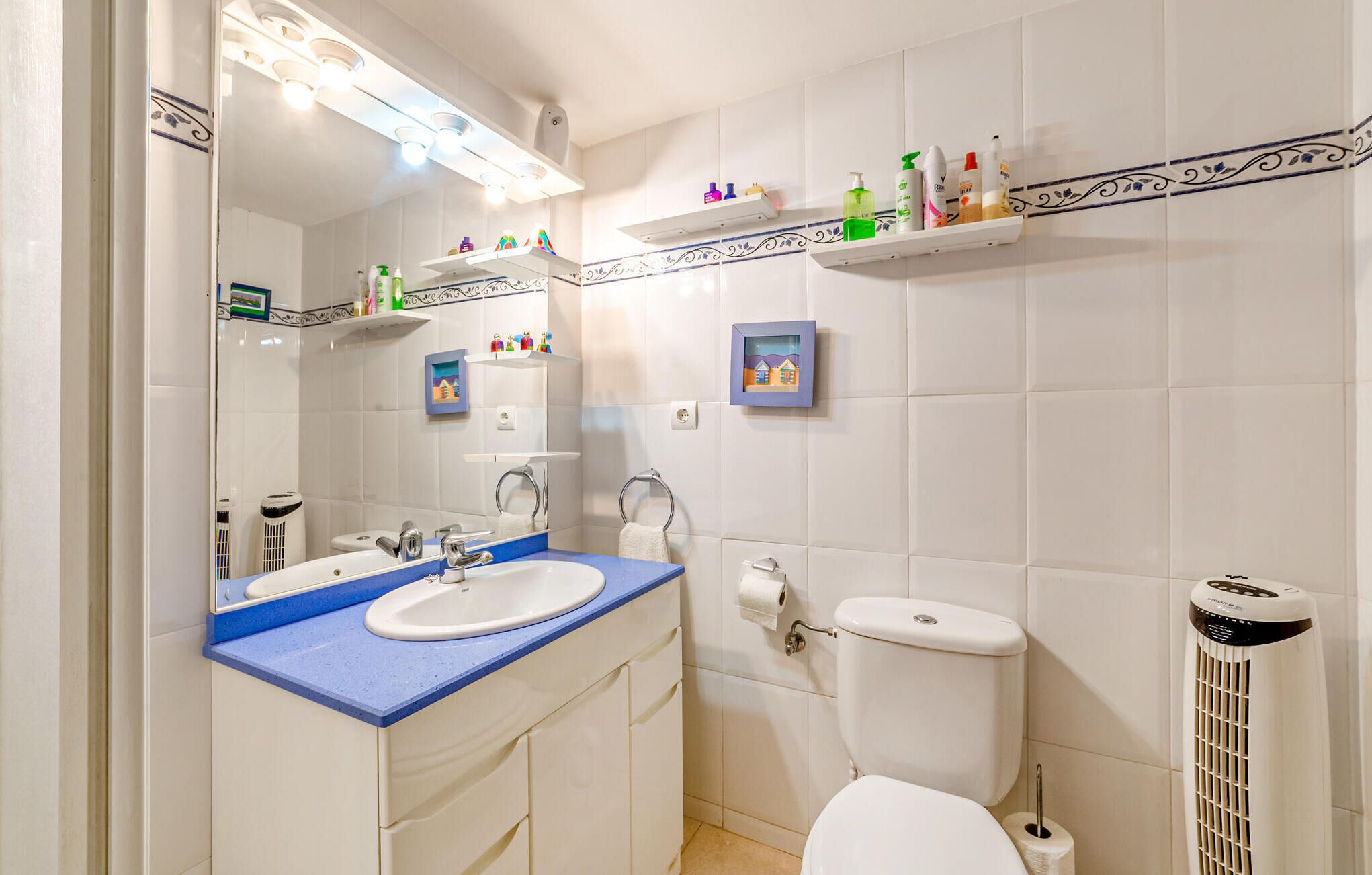 A bathroom with a sink, mirror, toilet, and shelves with toiletries.
