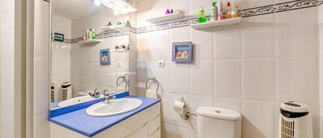 A bathroom with a sink, mirror, toilet, and shelves with toiletries.
