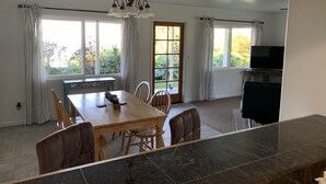 Un comedor con mesa y sillas de madera, una lámpara de araña y vistas amplias a través de grandes ventanales.