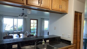 Una cocina con armarios de madera, encimera negra, pileta de acero inoxidable y un comedor con mesa y sillas.