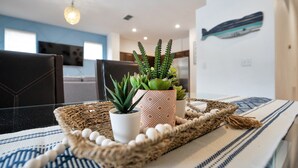 Een moderne woonkamer met een eethoek, met een geweven dienblad met potplanten, een patroonrijk vloerkleed en een op de muur bevestigde visdecoratie.