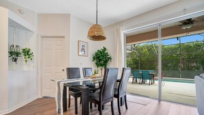 Een eethoek met een glazen tafel, donkere stoelen en een hanglamp.