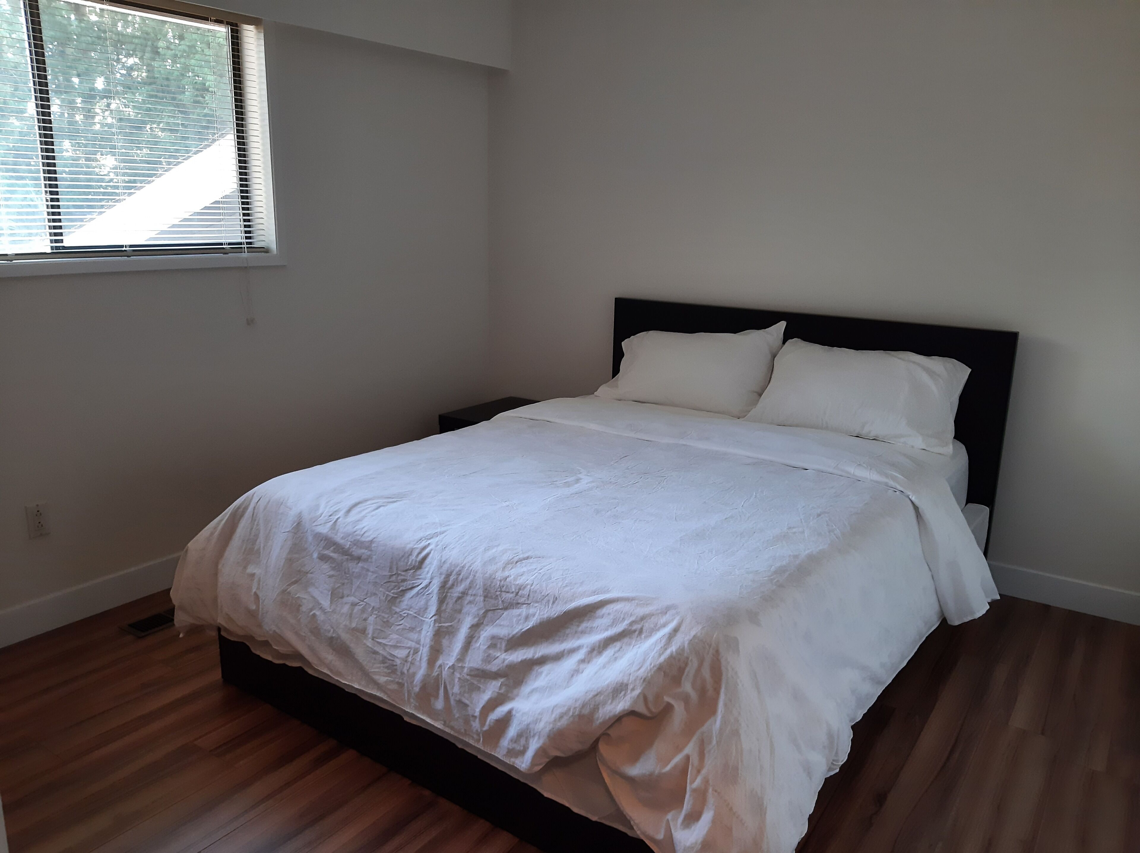 Une chambre à coucher avec un lit, une table de chevet, une fenêtre et un plancher en bois.