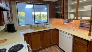 Une cuisine avec des meubles en bois, un fourneau blanc, un lave-vaisselle et une grande fenêtre donnant sur les arbres.