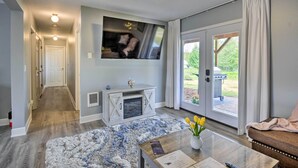 Ein modernes Wohnzimmer mit Kamin, Flachbildfernseher, Couchtisch mit Blumenvase und einer Schiebetür zu einer Terrasse.