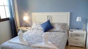 A neatly made bed with a blue pillow, two white towels, and a nightstand with a lamp and a small statue. - 4 bedroom LUXURY villa with AC, private heated pool, XBOX and all the amenities! (Castillo Caleta de Fuste)
