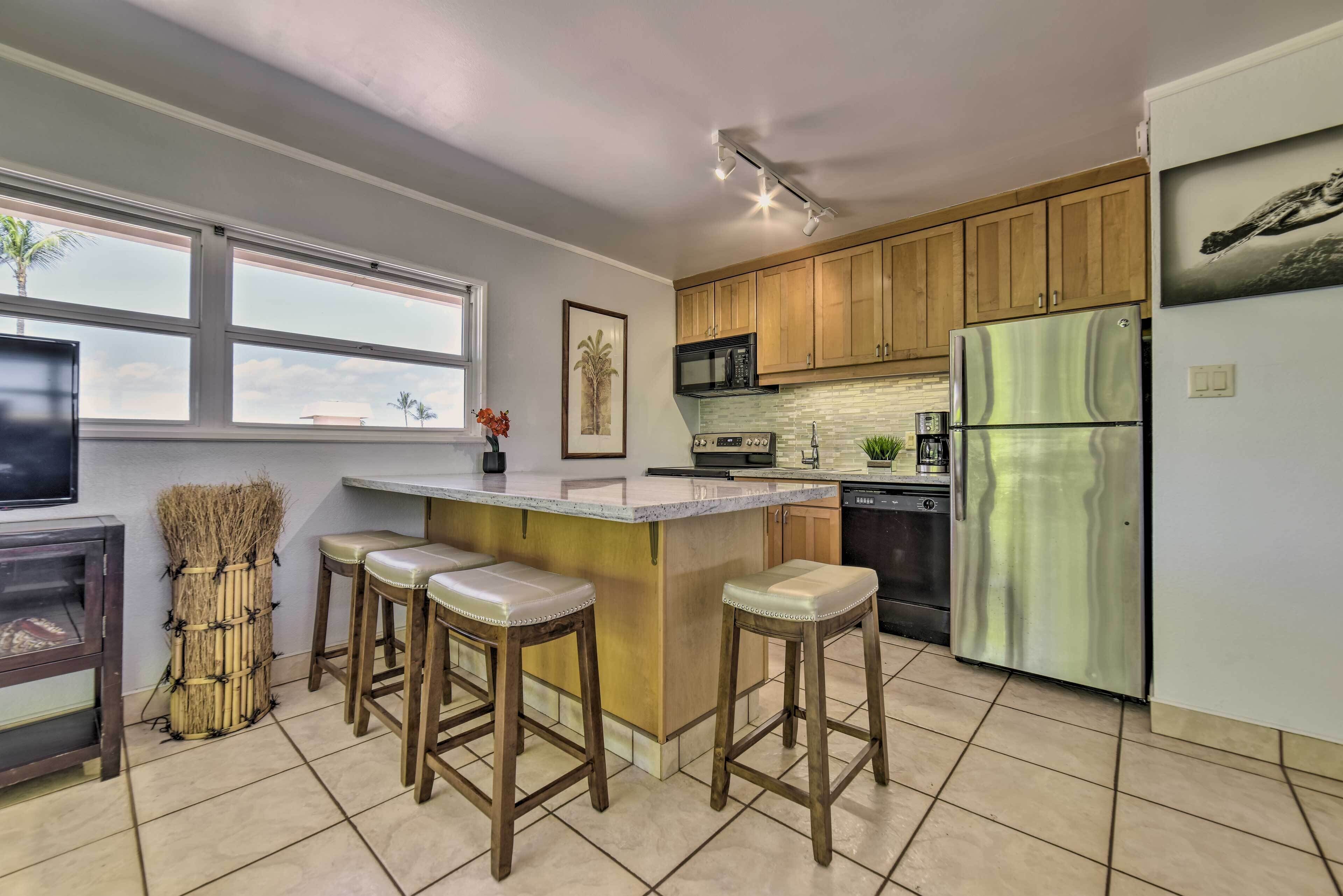A modern kitchen with wooden cabinets, a stainless steel refrigerator, a microwave, and a bar area with stools.