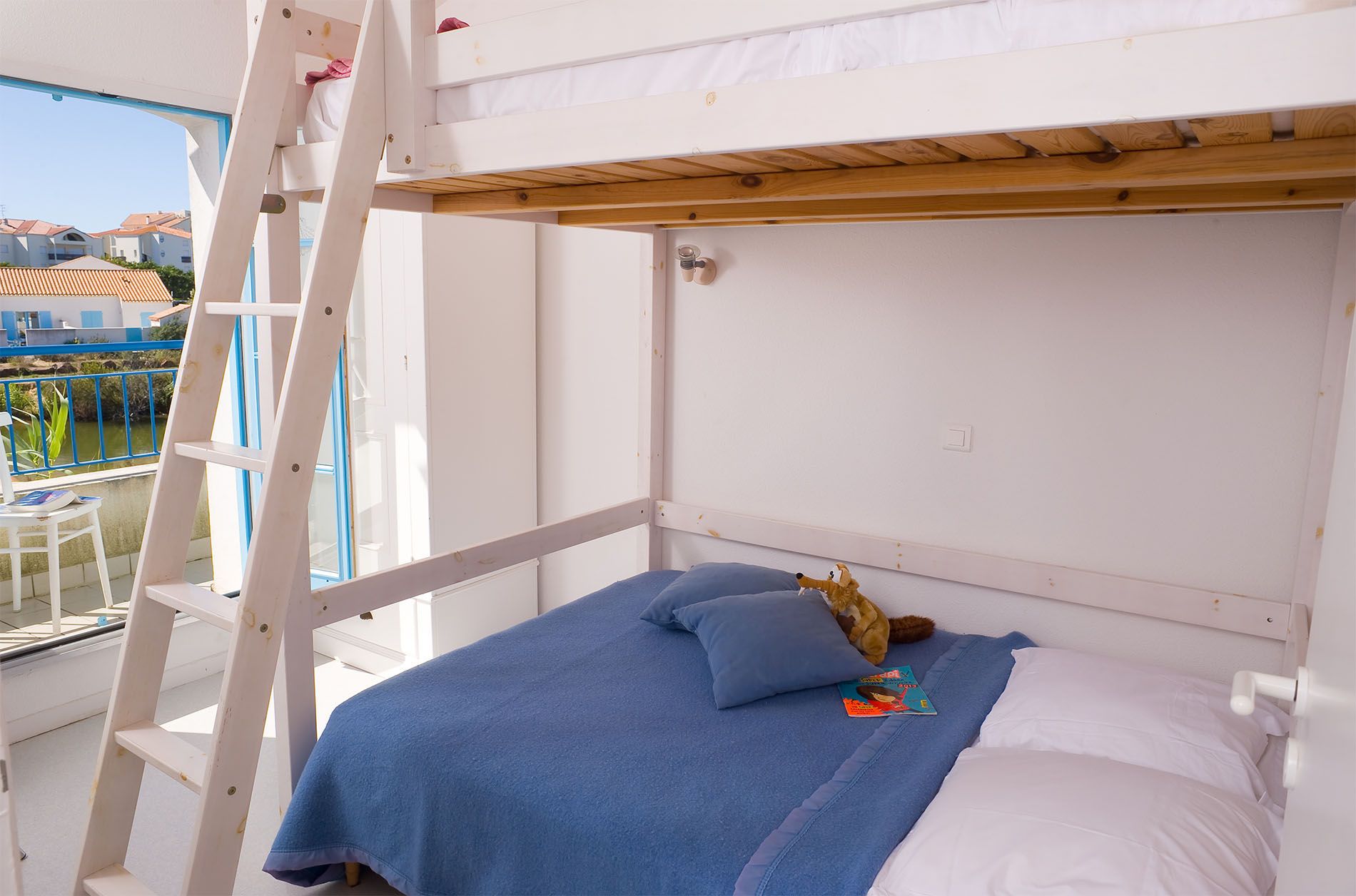 Una cama litera con escalera, una manta azul y una almohada.