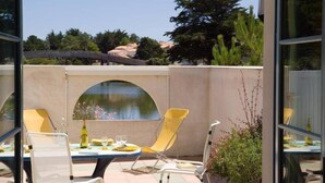 Un patio al aire libre con sillas amarillas y una mesa, una pequeña fuente de agua, y vistas a árboles y edificios al fondo.
