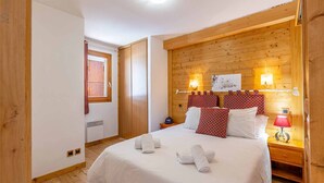 Ein gemütliches Schlafzimmer mit einem Holzkopfteil, einem großen Bett mit weißer Bettwäsche, zwei Nachttischlampen und einem Fenster mit Vorhängen.