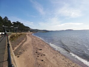 A coastal walkway with a sandy beach, a clear sky, and a distant ship. - Lovely 1 Bedroom condo with sea views. (Largs)