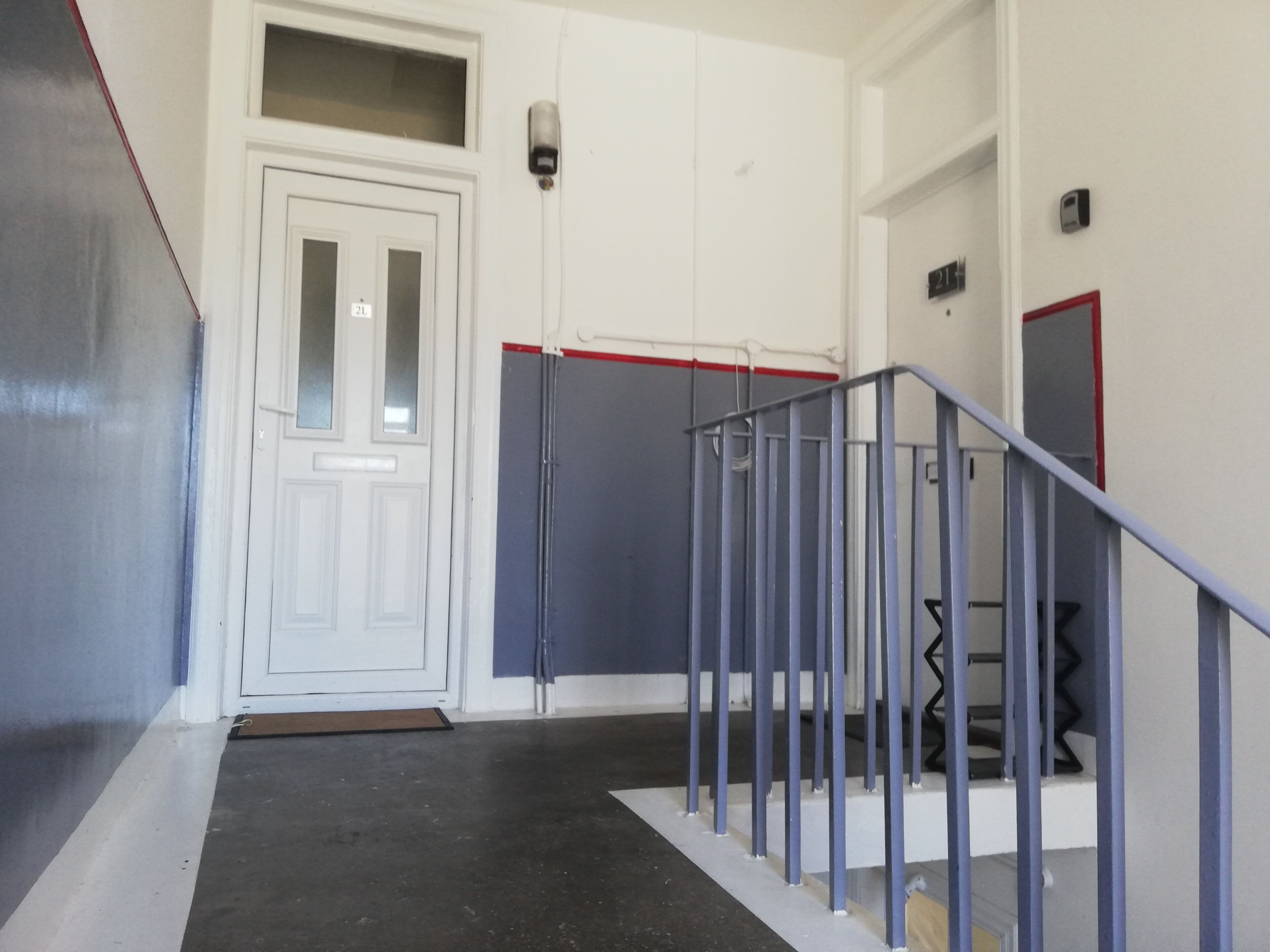 A hallway with a white door, a metal railing, and a red stripe on the wall.