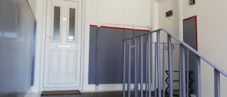 A hallway with a white door, a metal railing, and a red stripe on the wall.