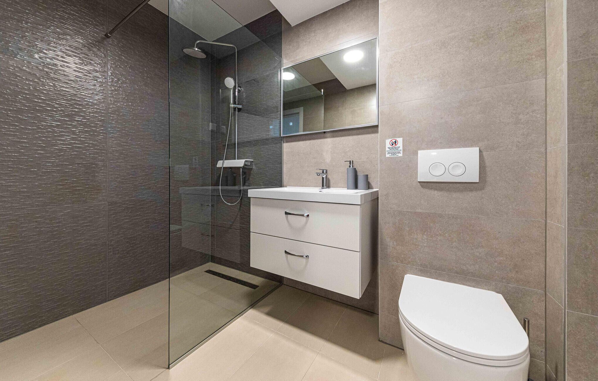 Une salle de bain moderne avec une douche à parois de verre, un lavabo blanc avec un miroir au-dessus et des toilettes.