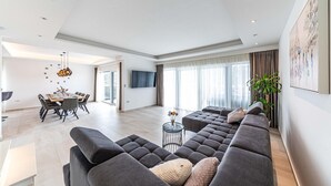 A modern living room with a large grey sectional sofa, a dining area with a wooden table and chairs, and a large window with curtains. - Gorgeous home in Marina (Marina)
