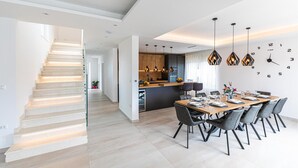 A modern kitchen with pendant lighting, a dining area with a wooden table and chairs, and a staircase with integrated lighting. - Gorgeous home in Marina (Marina)