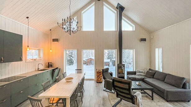 A spacious living area with a high ceiling, a fireplace, and large windows offering a view of a snowy landscape.