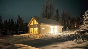 A snow-covered landscape with a house illuminated by warm lights.