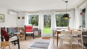 Een gezellige kamer met een eethoek, een bank en een stoel. Er zijn ramen met gordijnen, een vloerkleed en een hanglamp.
