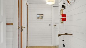 Een hal met witte houten wanden, een deur met een messing handgreep, een lijst met een afbeelding aan de muur en een hanglamp.