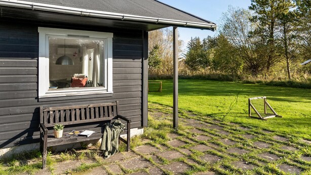 Een klein houten huisje met een raam, een bankje buiten en een gazon met een schommel.