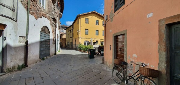 A narrow cobblestone street flanked by historic buildings with arched doorways and a yellow building with a wooden door.