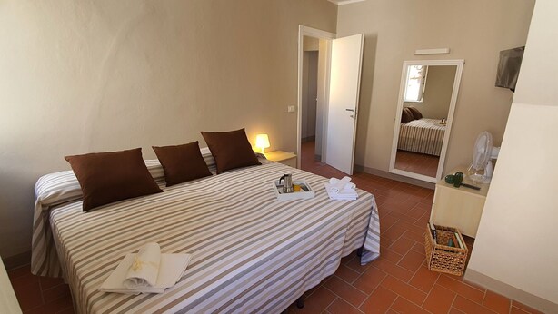 A hotel room with a bed, pillows, a bedside table with a lamp, a mirror, and a small basket. - Lovely apartment for 5 people with WIFI, A/C, TV and panoramic view (Lucca)