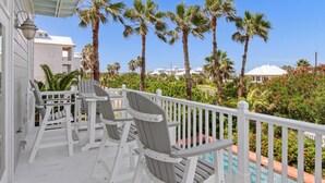 A balcony with white railings and two Adirondack chairs, overlooking a pool and palm trees. - Lotus Villa-Beautiful Straw paths through the pretty dunes. Look out tower! (South Padre Island)