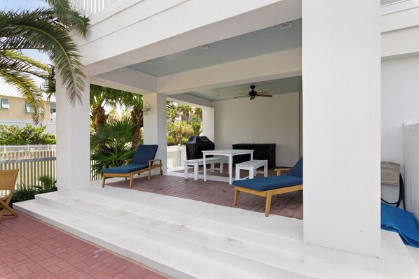 A covered outdoor seating area with a table and chairs, a grill, and a view of the surrounding greenery.