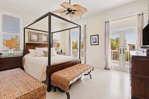 A four-poster bed with a wooden frame, a bench, and a woven basket in a room with a balcony.