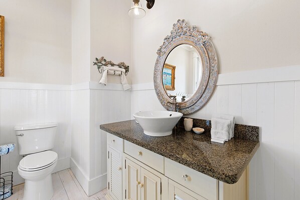 A bathroom with a white toilet, a sink with a decorative mirror, and a towel rack.