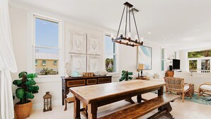 A spacious living room with a wooden dining table, wicker chairs, and a hanging light fixture. - Lotus Villa-Beautiful Straw paths through the pretty dunes. Look out tower! (South Padre Island)